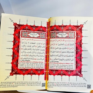 May include: Open book with Arabic text and ornate red and gold borders. The pages display verses from the Quran, with Arabic script and translations. The book is open to two facing pages.