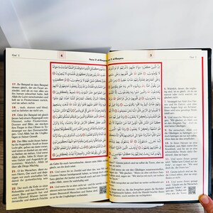 May include: Open book with Arabic text. The pages are yellowed, and the text is in black. The book is open to a page with text and a decorative border. The book is likely a religious text, possibly the Quran.