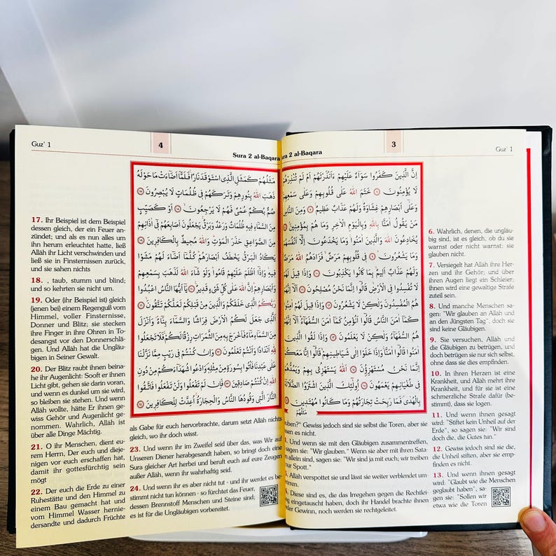 May include: Open book with Arabic text. The pages are yellowed, and the text is in black. The book is open to a page with text and a decorative border. The book is likely a religious text, possibly the Quran.