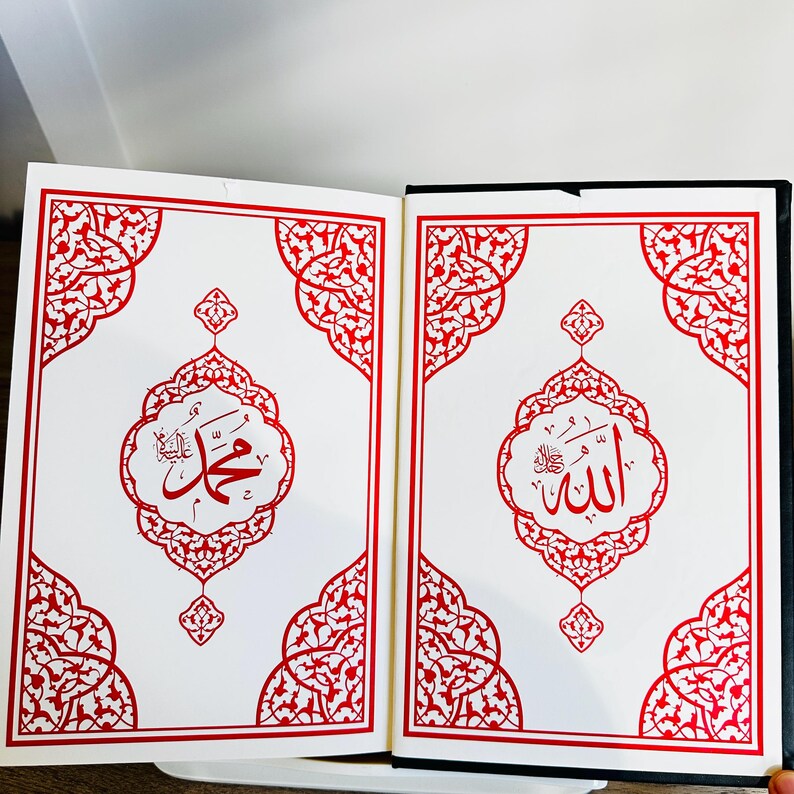 May include: Open book with white pages featuring red ornate designs and Arabic calligraphy. The left page displays the name "Muhammad" in red script within a decorative frame. The right page shows the name "Allah" in red script.