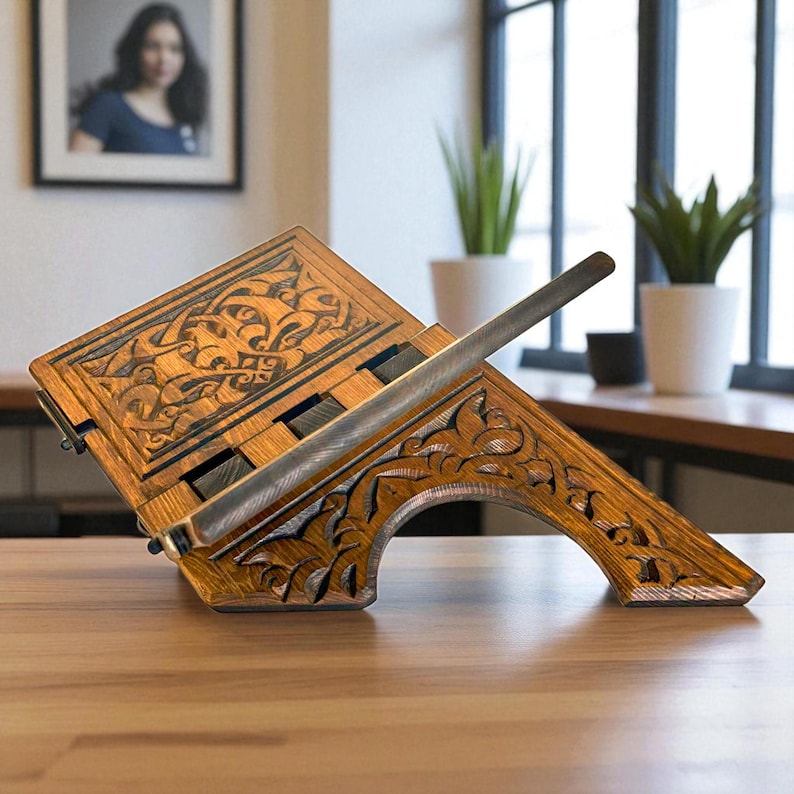 Puede incluir: Un atril de madera con intrincados dise&ntilde;os tallados. El atril est&aacute; inclinado, con una barra de metal para sujetar las p&aacute;ginas abiertas. La madera tiene un tono c&aacute;lido y natural, y los grabados presentan patrones arremolinados. El atril est&aacute; sobre una superficie de madera.
