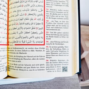 May include: Open book with Arabic text and German translation. The pages are yellowed, and the text is in black. The book is open to a page with a red border. The text is in both Arabic and German.