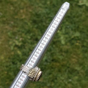 Peut inclure: Une bague en argent avec un anneau textur&eacute; et une grosse pierre pr&eacute;cieuse rouge fonc&eacute; est pr&eacute;sent&eacute;e sur un baguier. Le baguier a des mesures en tailles fran&ccedil;aises. Le fond est vert flou.