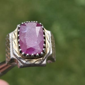 Peut inclure: Une bague en argent orn&eacute;e d'un grand rubis rectangulaire &agrave; facettes. Le rubis est d'un rouge-ros&eacute; profond. La bague pr&eacute;sente un motif d&eacute;taill&eacute; et textur&eacute; autour de la pierre et sur le corps.