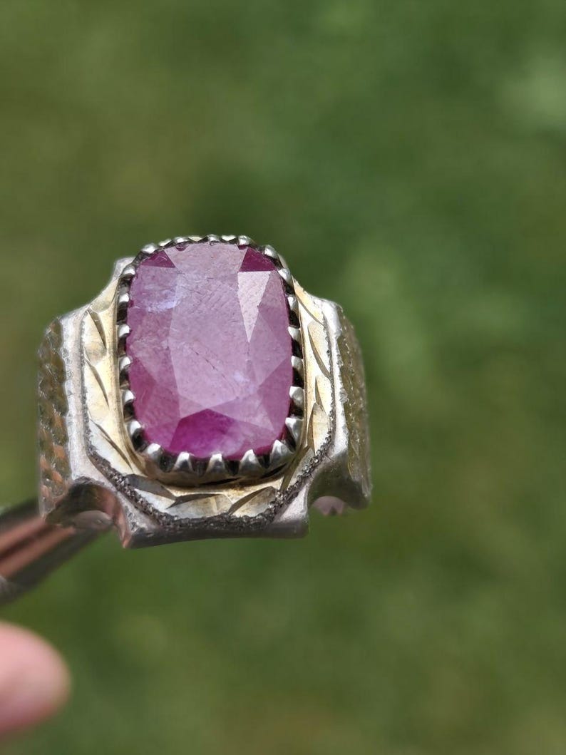 Peut inclure: Une bague en argent orn&eacute;e d'un grand rubis rectangulaire &agrave; facettes. Le rubis est d'un rouge-ros&eacute; profond. La bague pr&eacute;sente un motif d&eacute;taill&eacute; et textur&eacute; autour de la pierre et sur le corps.
