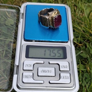 Peut inclure: Une bague argent&eacute;e avec une grosse pierre pr&eacute;cieuse ovale rouge fonc&eacute; est pr&eacute;sent&eacute;e sur une balance num&eacute;rique. La balance affiche un poids de 17,55. La bague a un design orn&eacute; et textur&eacute;.