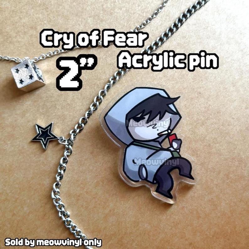 Op de afbeelding: Een 5 cm acrylspeld met een stripfiguur in een grijze hoodie, die een rood voorwerp vasthoudt. De speld heeft de tekst "Cry of Fear Acrylic pin". Een zilveren ketting met een ster- en dobbelsteenhanger is ook zichtbaar.