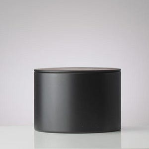 May include: A matte black cylindrical container with a wooden lid. The container is a solid color and sits on a white surface. The design is simple and modern, suitable for storage or display.