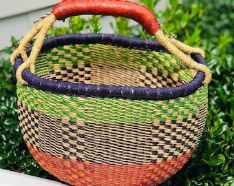 Könnte beinhalten: Ein geflochtener Korb mit einem braunen Ledergriff. Der Korb ist aus natürlichen Materialien gefertigt und hat ein grün-gelb-rotes Muster.