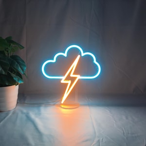 May include: A neon sign shaped like a cloud with a lightning bolt. The cloud is outlined in blue, and the lightning bolt is orange. The sign is on a clear stand and emits a warm glow.