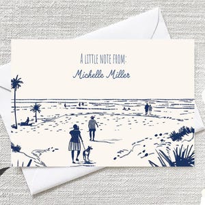 May include: A white card with a blue illustration of a beach scene with people walking on the sand. The text "A little note from: Michelle Miller" is printed in blue at the top of the card.