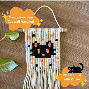 以下が含まれることがあります： 黒猫のデザイン、オレンジとピンクのアクセント、木の棒が付いたマクラメの壁掛け。テキスト「Create your own Cat Wall Hanging!」と「PDF Tutorial with Videos」が含まれています。