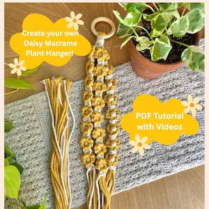 May include: A handmade daisy macrame plant hanger in yellow and white. The plant hanger features a wooden ring at the top and daisy flower details. The text "Create your own Daisy Macrame Plant Hanger!" is in a yellow bubble.