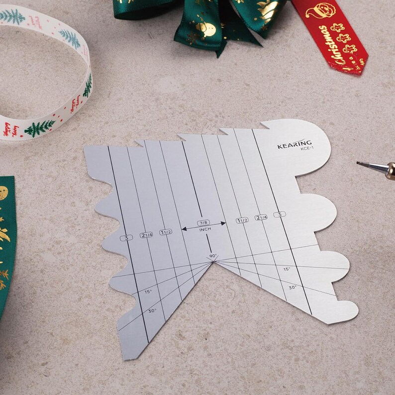 May include: A silver metal bow maker tool with measurements in inches. The tool has a tree-like shape with curved edges and is labeled "KEARING KCE-1". Ribbons in green, red, and white are in the background, suggesting a holiday theme.