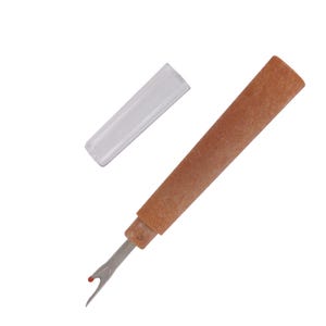 May include: A seam ripper with a brown handle and a clear plastic cap. The metal blade has a red tip. This tool is used for removing stitches from fabric.