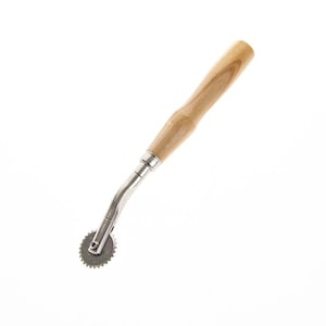 May include: A sewing tracing wheel featuring a light brown wooden handle with a smooth, cylindrical shape and a silver-colored metal shaft that curves slightly to connect to a small, circular, serrated metal wheel at the bottom end.