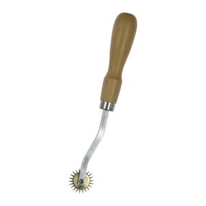 May include: A tracing wheel featuring a light brown wooden handle, a silver-toned metal shaft, and a small brass-colored serrated wheel at the end. The tool is designed with a slightly bent neck connecting the handle to the spiked circular wheel.