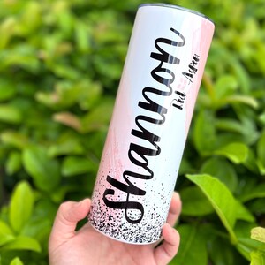 以下が含まれることがあります： ピンクと白のグラデーションデザインと黒のグリッターが付いた白いタンブラー。タンブラーには「Shannon」という名前と「Red Aspen」というテキストが書かれています。