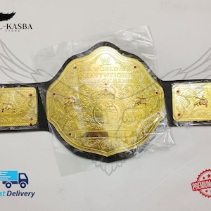 Puede incluir: Un cinturón de campeonato de color dorado con correas de cuero negro. La placa central presenta el texto "World Heavyweight Wrestling Champion" y una corona. Las placas laterales también son doradas y tienen un diseño decorativo.