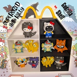 May include: A split-color white and black shelf shaped like the McDonald's golden arches, displaying various Hello Kitty and Godzilla character figurines. The shelf features the text SUPERSIZED Hello Kitty Godzilla Shelf.