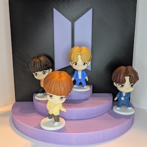 Könnte beinhalten: Eine Präsentation mit vier Figuren im Chibi-Stil mit braunen und blonden Haaren, die jeweils Anzüge in verschiedenen Farben tragen. Die Figuren stehen auf einer gestuften, lavendelfarbenen Plattform vor einem schwarzen Hintergrund mit einem lavendelfarbenen Logo.