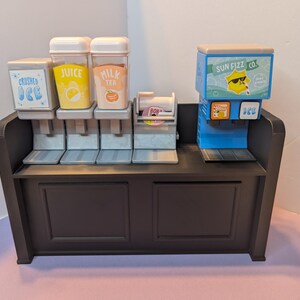 May include: A miniature beverage station with a dark brown cabinet and multiple dispensers. The dispensers include options for crushed ice, juice, milk tea, and a Sun Fizz Co. soda machine. The station is designed with a playful, cartoonish aesthetic.
