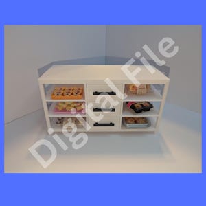 Op de afbeelding: Een witte miniatuur bakkerij vitrinekast met drie planken en drie lades. De planken bevatten diverse miniatuurgebakjes. De tekst bovenaan luidt "Digitale bestand download" en de tekst onderaan luidt "U ontvangt geen fysiek item."