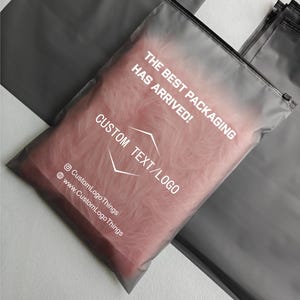 Könnte beinhalten: Eine transparente, mattierte Plastikverpackungstasche mit Reißverschluss. Die Tasche enthält rosa, flauschiges Material. Weißer Text auf der Tasche lautet "THE BEST PACKAGING HAS ARRIVED!" und "CUSTOM TEXT/LOGO". Die Tasche zeigt auch Social-Media-Handles.