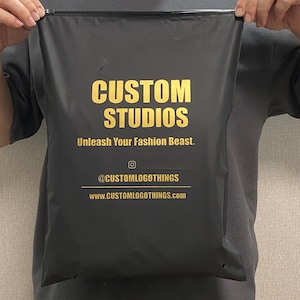 May include: Black shipping bag with gold text that reads "CUSTOM STUDIOS" and "Unleash Your Fashion Beast." Below the text is the Instagram handle "@CUSTOMLOGOTHINGS" and the website "www.CUSTOMLOGOTHINGS.com."