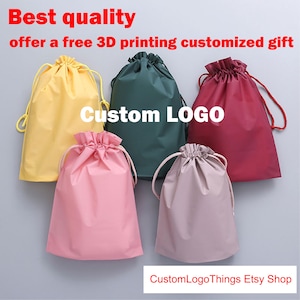 May include: Five drawstring bags in yellow, green, red, pink, and mauve. The bags have a gathered top and a drawstring closure. Text on the image reads "Best quality, offer a free 3D printing customized gift" and "Custom LOGO".