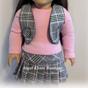 Op de afbeelding: Een roze longsleeve shirt met een zwart-wit geruit vest en een bijpassende rok. De rok heeft plooien en de tekst "Angel Kisses Boutique" is op de voorkant gedrukt.