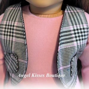 Op de afbeelding: Een zwart-wit geruit vest met roze accenten. Het vest heeft aan elke kant een zak. Het vest wordt gedragen door een pop.