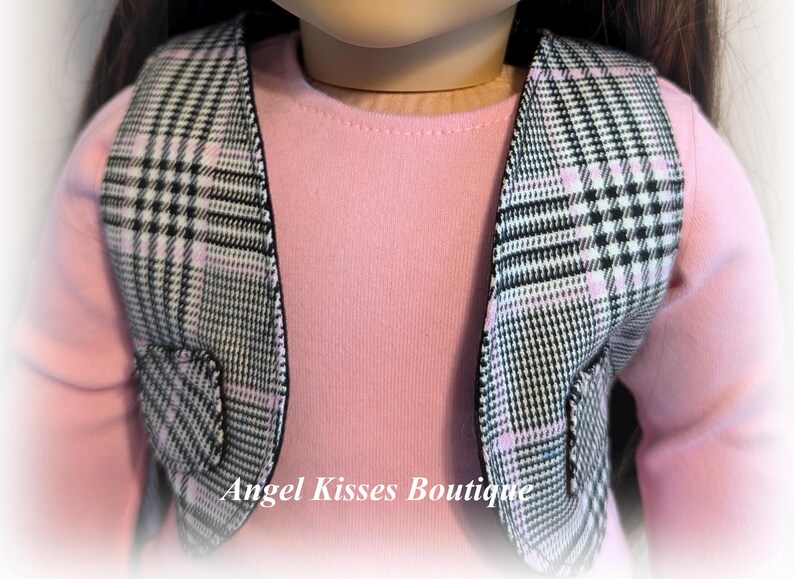 Op de afbeelding: Een zwart-wit geruit vest met roze accenten. Het vest heeft aan elke kant een zak. Het vest wordt gedragen door een pop.