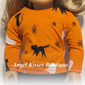 May include: Orange long-sleeved shirt with Halloween-themed graphics. The shirt features black cat and spiderweb designs, along with white ghost illustrations. The text "Angel Kisses Boutique" is visible on the shirt.