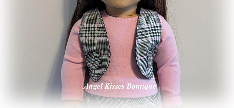 Op de afbeelding: Een zwart-wit geruit vest met roze bies en hartvormige details. Het vest wordt gedragen over een roze longsleeve. Angel Kisses Boutique.