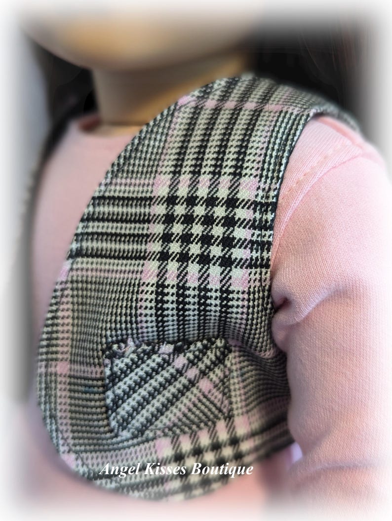 Op de afbeelding: Een zwart-wit geruit vest met roze accenten. Het vest heeft een klein zakje aan de voorkant. Het vest wordt gedragen over een roze shirt.