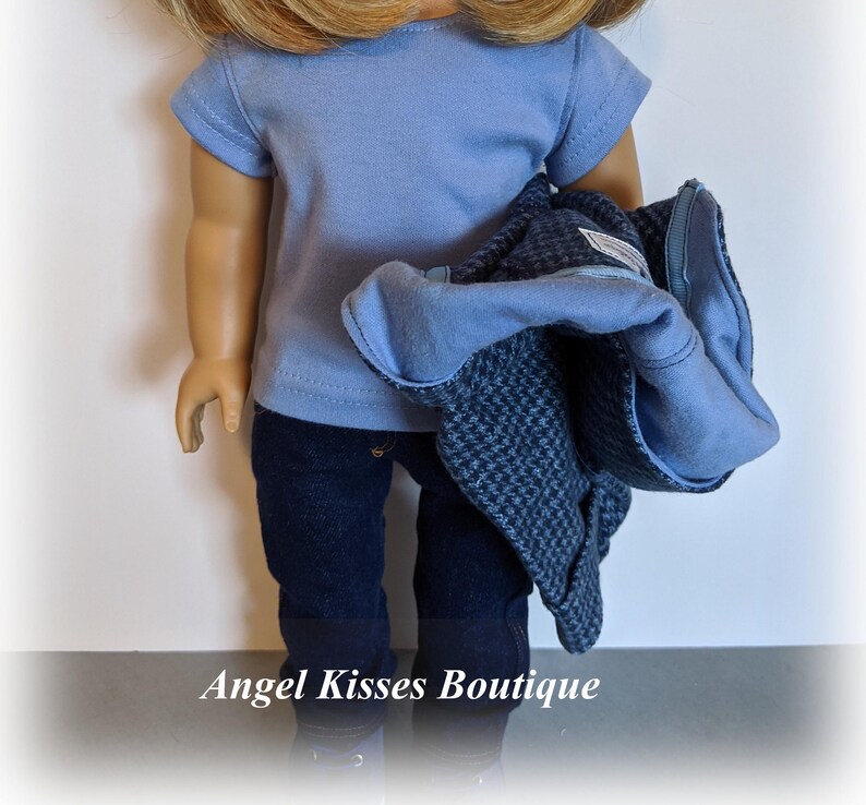 May include: A doll wearing a light blue t-shirt, dark blue jeans, and a dark blue and grey jacket.