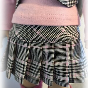 Op de afbeelding: Een zwart-wit geruite rok met roze accenten. De rok heeft plooien en is gemaakt van een zachte, comfortabele stof.
