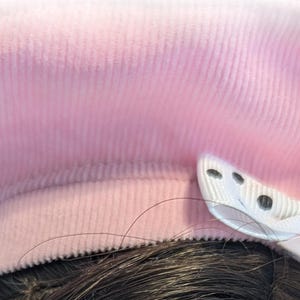 Op de afbeelding: Een roze corduroy baret met een witte strik versierd met zwarte stippen.