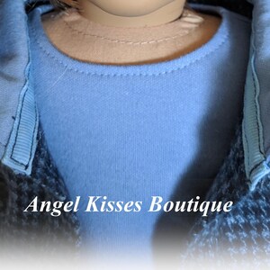 May include: A close-up of a blue shirt with a black and blue jacket. The jacket has a collar that is folded down. The text "Angel Kisses Boutique" is visible in the image.