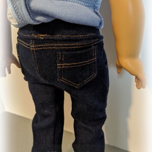 May include: A pair of dark blue denim jeans with orange stitching. The jeans have a back pocket with orange stitching.