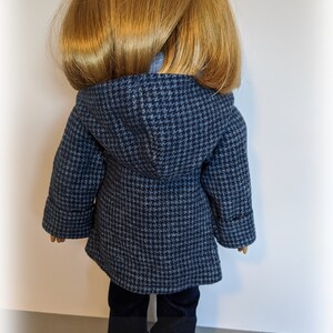 May include: A blue and white houndstooth hooded coat for a doll. The coat has long sleeves and a zip closure. The doll is wearing blue jeans.