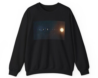 Peut inclure: Sweat-shirt noir avec un motif céleste. Le graphisme représente une ligne de planètes et de lunes, avec le soleil à droite. Le fond est bleu foncé avec des étoiles.