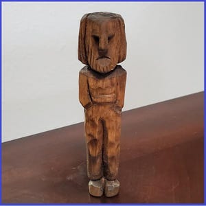 May include: A wooden carving of a person with a long beard and a serious expression. The carving is made of a light brown wood and has a rustic appearance.