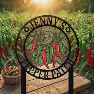 Puede incluir: Estaca de jardín de metal negro con el texto "Jenny's Pepper Patch" en un diseño circular, con pimientos rojos y verdes. Una cesta de pimientos se encuentra sobre una superficie de madera, con un fondo de plantas de pimiento.