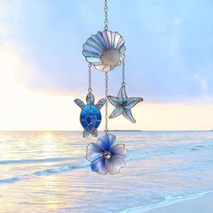 May include: A hanging stained glass mobile featuring a seashell, starfish, turtle, and flower. The sea-themed ornaments are in shades of blue and white, suspended by chains. The background shows a beach scene.
