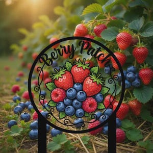 May include: A black metal garden stake with the words "Berry Patch" in a circular design. The design features illustrations of strawberries, blueberries, and raspberries. The background shows a berry patch with ripe strawberries and blueberries.