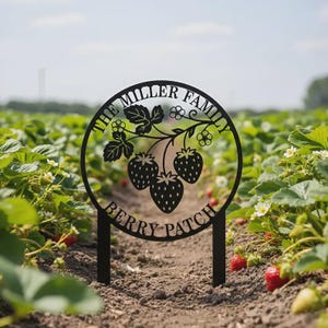 Könnte beinhalten: Schwarzes Metallschild mit den Worten "THE MILLER FAMILY BERRY PATCH" in einem kreisförmigen Design. Das Schild zeigt eine Erdbeerpflanze mit drei Beeren und befindet sich in einem Erdbeerfeld.