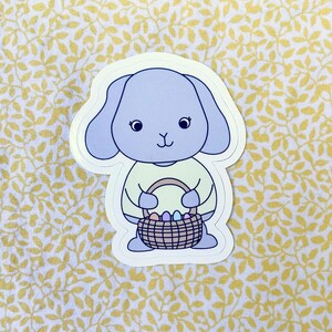 Poppy verzamelt eieren in haar paasmandje, schattig blauwgrijs konijntje sticker voor dagboek, laptop, telefoon, sticker en meer
