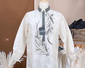 May include: Off-white long-sleeved shirt with intricate black floral embroidery. The shirt features a patterned collar and a tag that reads "HARKO". The shirt is displayed on a mannequin.